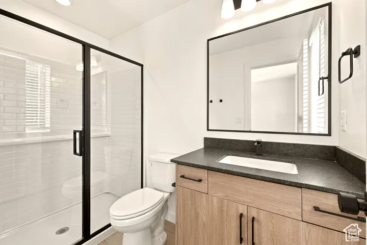 Bathroom featuring a glass-enclosed shower with subway tile surround, wood-finish vanity with a dark composite countertop, integrated rectangular sink, and matte black hardware
