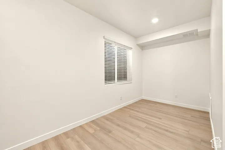 Neutral interior space featuring wood-finish flooring, crisp white walls, and a recessed ceiling light