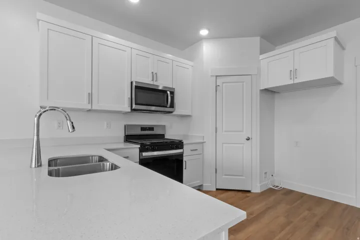 Kitchen featuring white shaker cabinetry, stainless steel appliances, a dual basin undermount sink, a chrome pull-down faucet, and wood-finish flooring