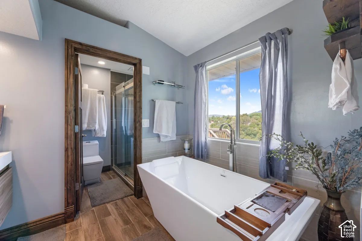 Freestanding soaking tub with floor-mounted faucet, wood-finish flooring, and a glass-enclosed shower