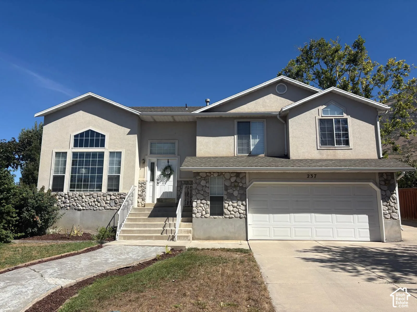 Exterior featuring a stucco finish, stone accents, multiple window styles, an attached two-car garage, and a concrete driveway