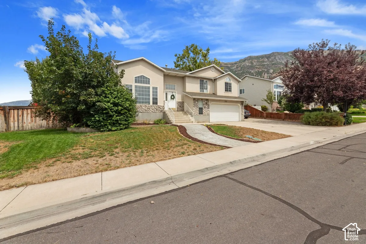 Multi-story exterior with stone veneer accents, an integrated garage, a paved driveway, and mature landscaping