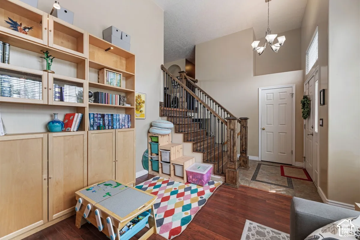 Entryway featuring a wood-finish flooring, staircase with wood newel posts and black iron balusters, built-in shelving units, and a chandelier