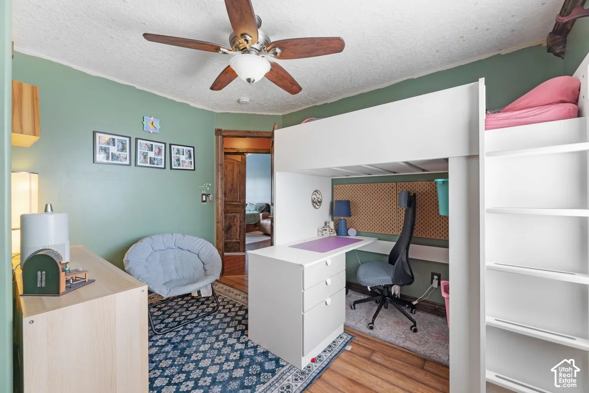 Wood-finish flooring, ceiling fan, built-in loft bed with integrated desk and shelving, and a wood-paneled door