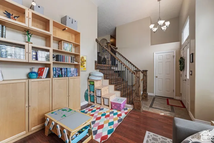 Entryway featuring a wood-finish flooring, staircase with wood newel posts and black iron balusters, built-in shelving units, and a chandelier