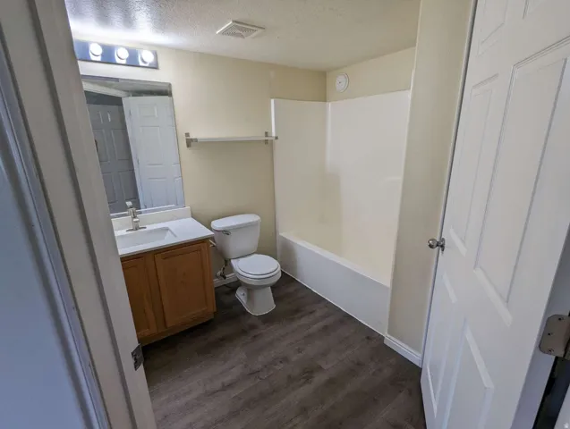 Bathroom featuring wood-finish flooring, a single vanity with an integrated sink, a toilet, and a combined tub and shower unit