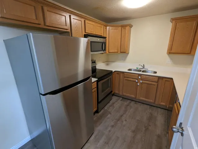 Kitchen featuring wood-finish cabinetry, stainless steel appliances, a double basin sink, light-toned countertops, and wood-finish flooring