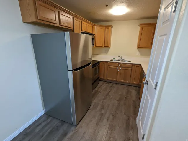 Stainless steel refrigerator, built-in cabinetry, wood-finish flooring, stainless steel sink, and light-toned countertops