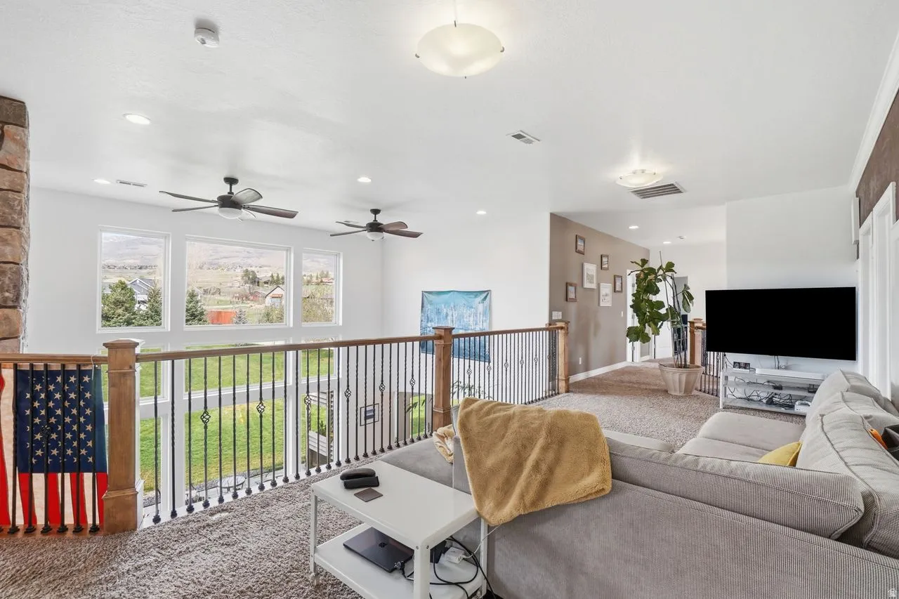 Open concept loft space featuring a stone-clad pillar, decorative metal railing, recessed lighting, and multiple ceiling fans