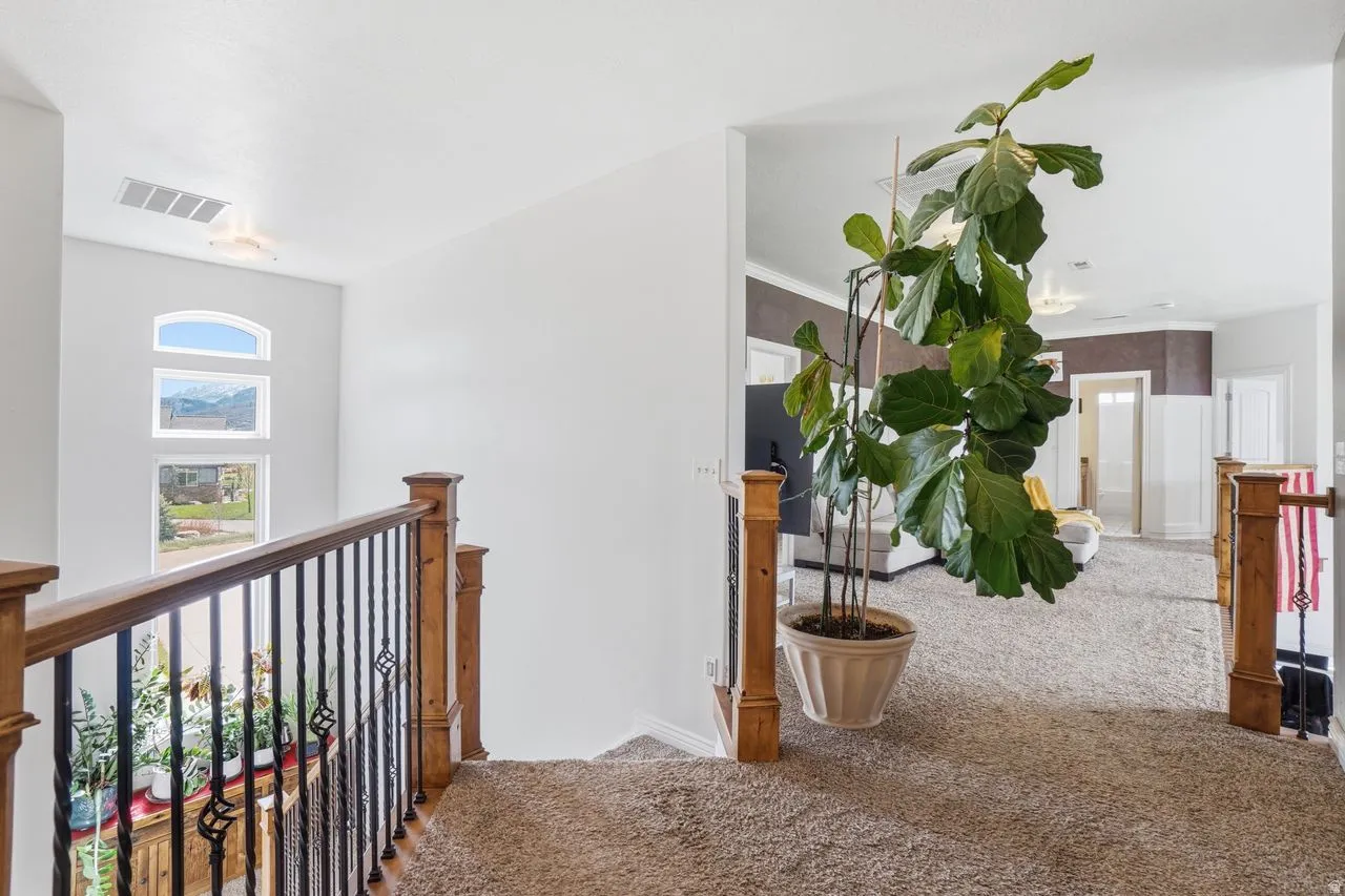 Carpeted upper landing featuring a wood and wrought iron railing, arched window, and recessed lighting
