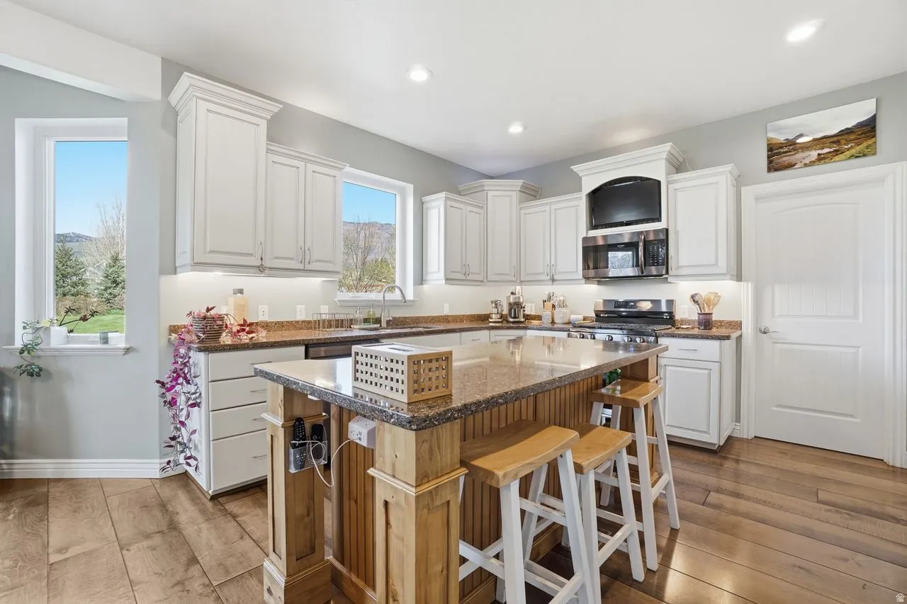 Kitchen featuring white cabinetry, granite countertops, wood-finish flooring, a center island with bar seating, and stainless steel appliances