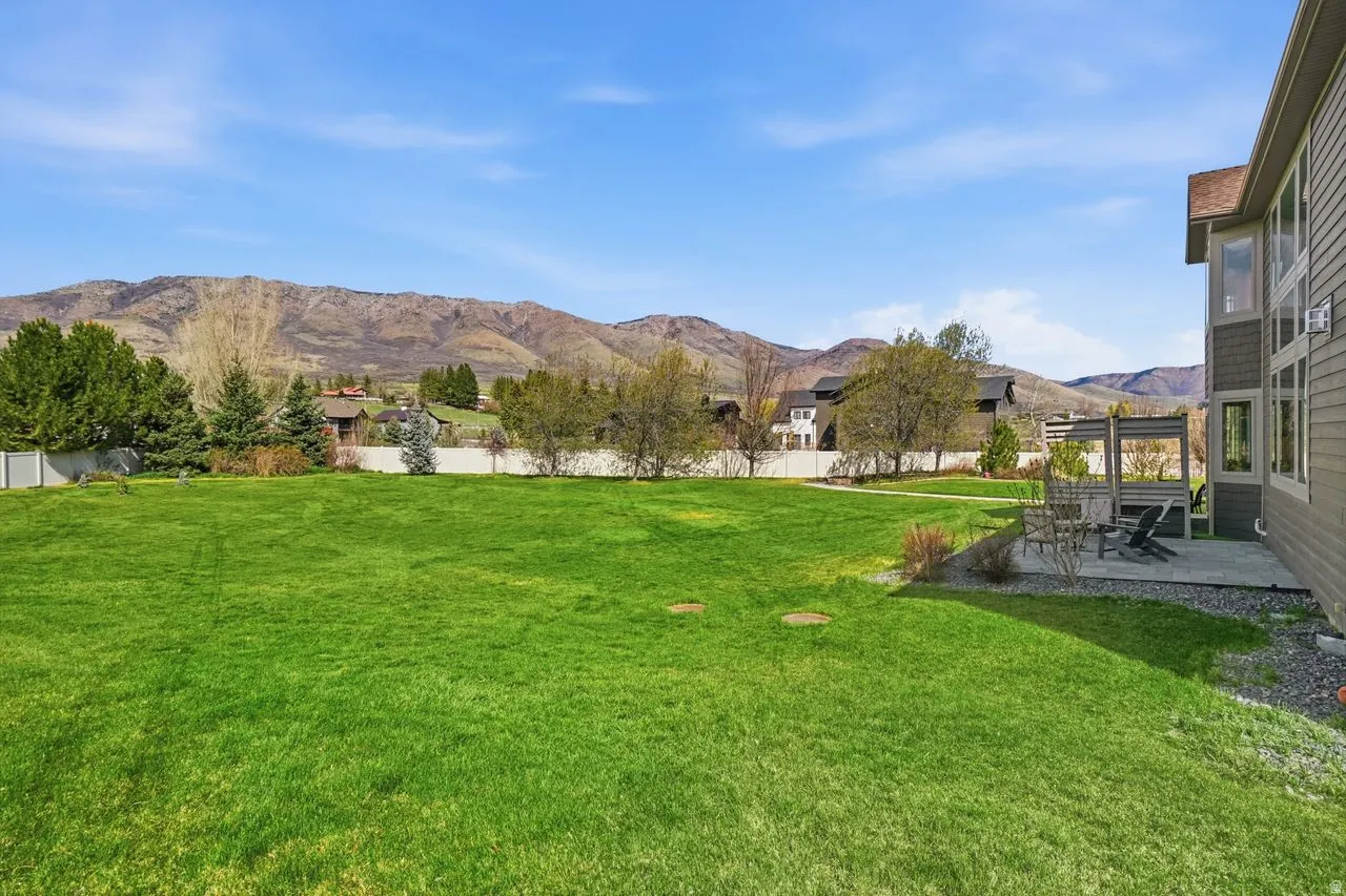 Expansive green lawn with mountain backdrop, concrete patio, and exterior siding