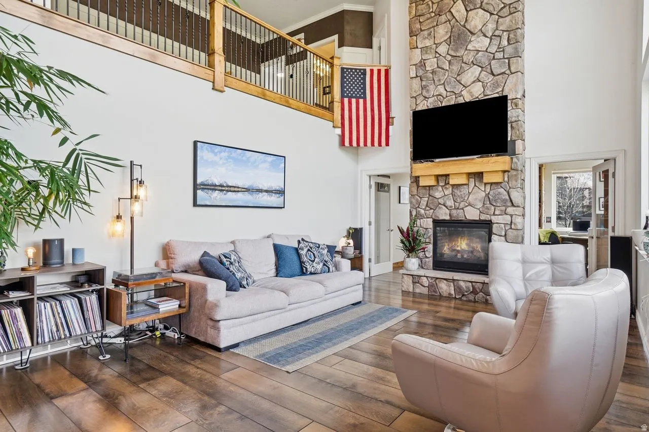 Vaulted ceilings with a wood and metal railing loft, stone fireplace with a wood mantle, wood-finish flooring, and white walls