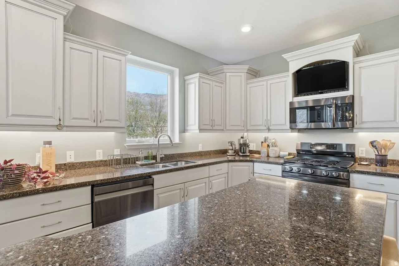 White shaker cabinetry, stainless steel appliances, dark speckled countertops, undermount sink, and a built-in microwave