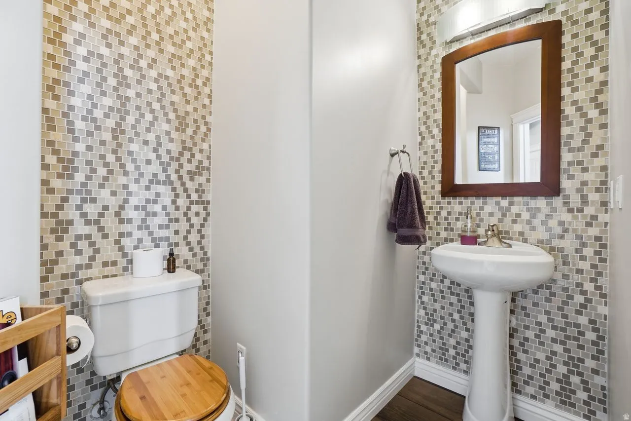 Pedestal sink with mosaic tile accent wall, wood-frame mirror, and wall-mounted light fixture