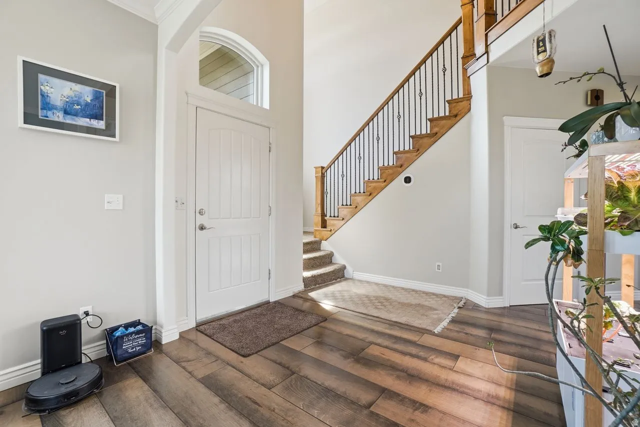 Wood-finish flooring, staircase with wood treads and wrought iron balusters, white paneled entry door with arched transom, white paneled interior doors, and crown molding