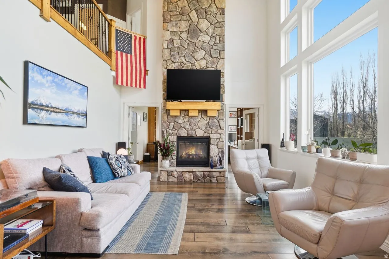 Vaulted ceilings with abundant natural light, a stone-clad fireplace with a wood mantel, wood-finish flooring, and an open-tread staircase with wrought iron balusters