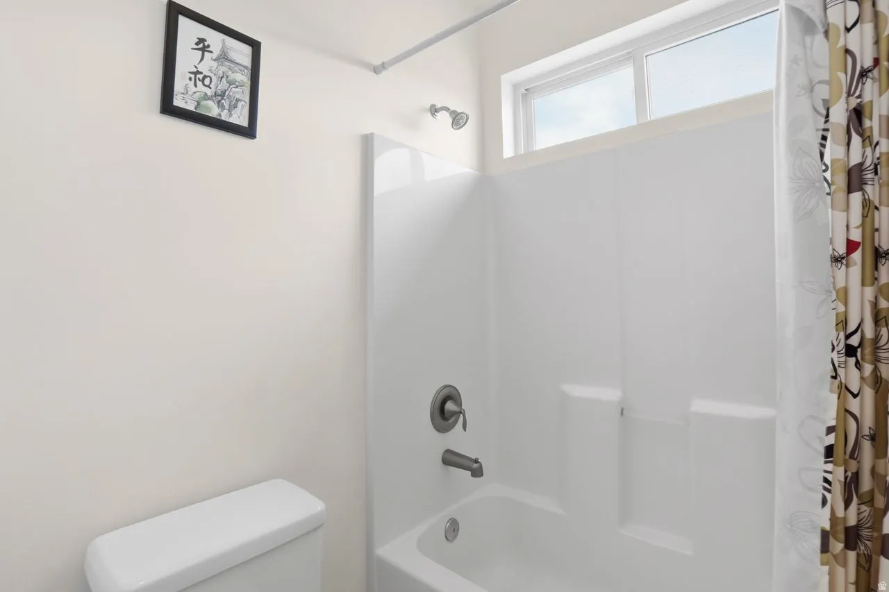 White toilet, white shower/tub combination, overhead window, and wall-mounted shower head