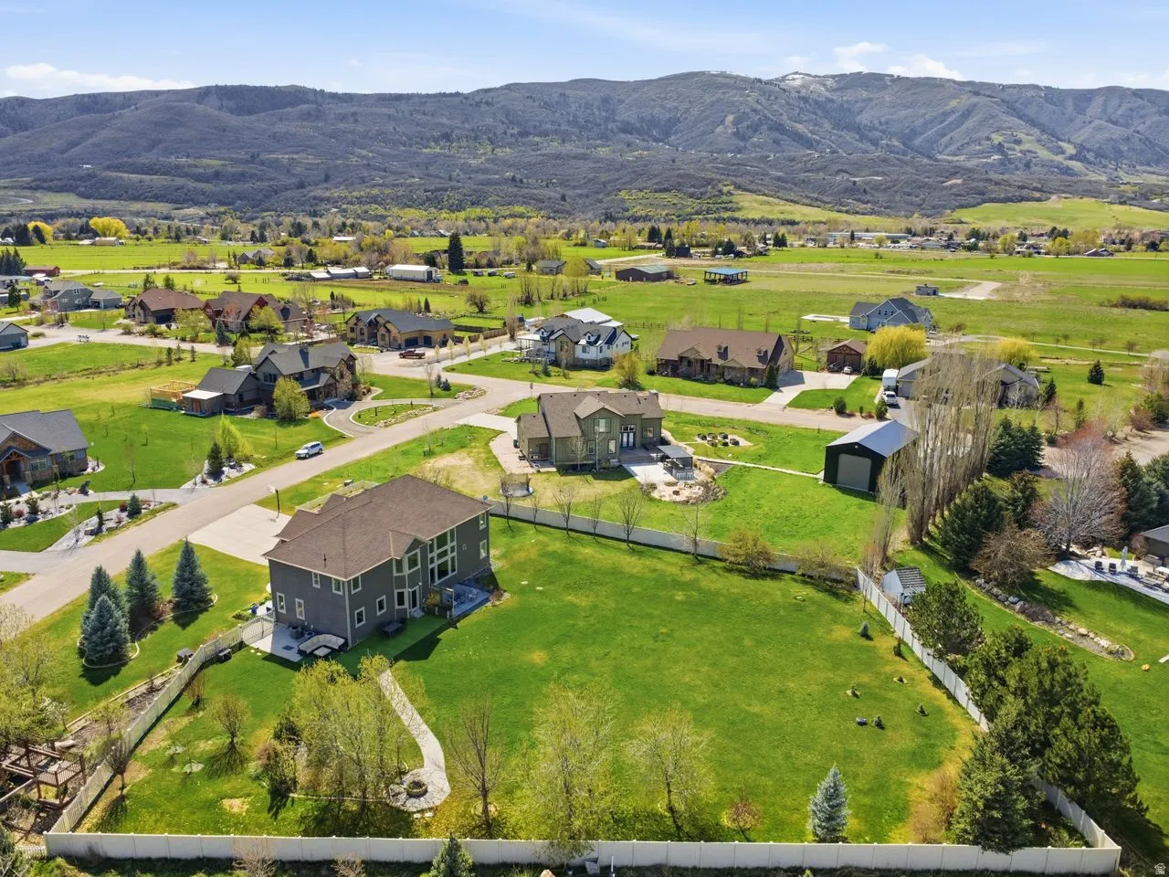 Expansive green property with a fenced perimeter, mature trees, and a paved patio area
