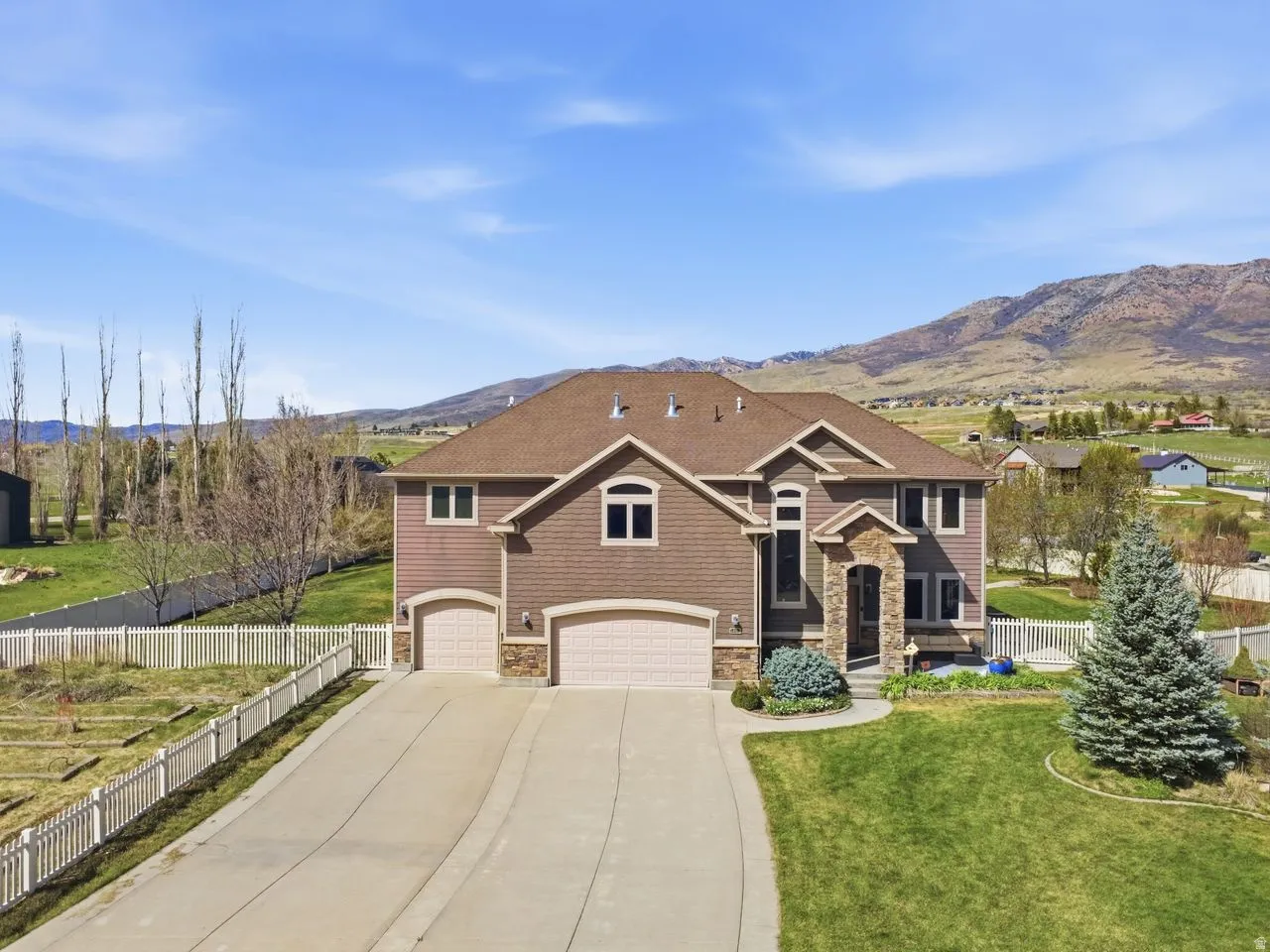 Two-story home with a stone and siding exterior, featuring a three-car garage, a concrete driveway, and a front lawn with a mature evergreen