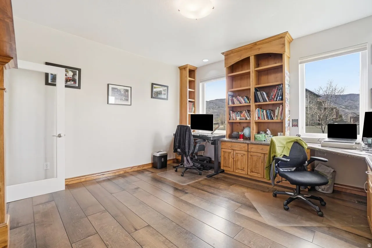 Spacious room featuring wood-finish flooring, built-in shelving, custom cabinetry, multiple windows, and a frosted glass door