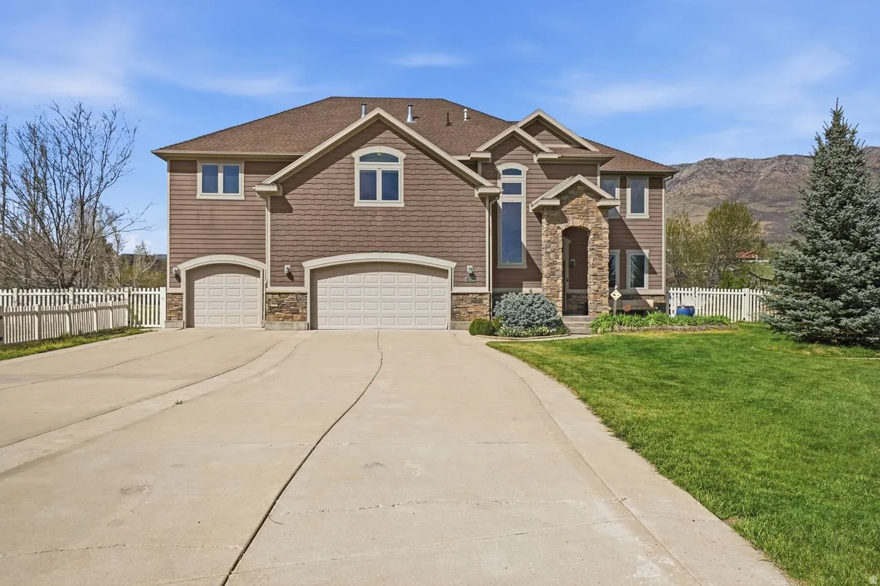 Two-story exterior with a brown siding finish and stone accents, featuring an arched entry and a multi-car driveway