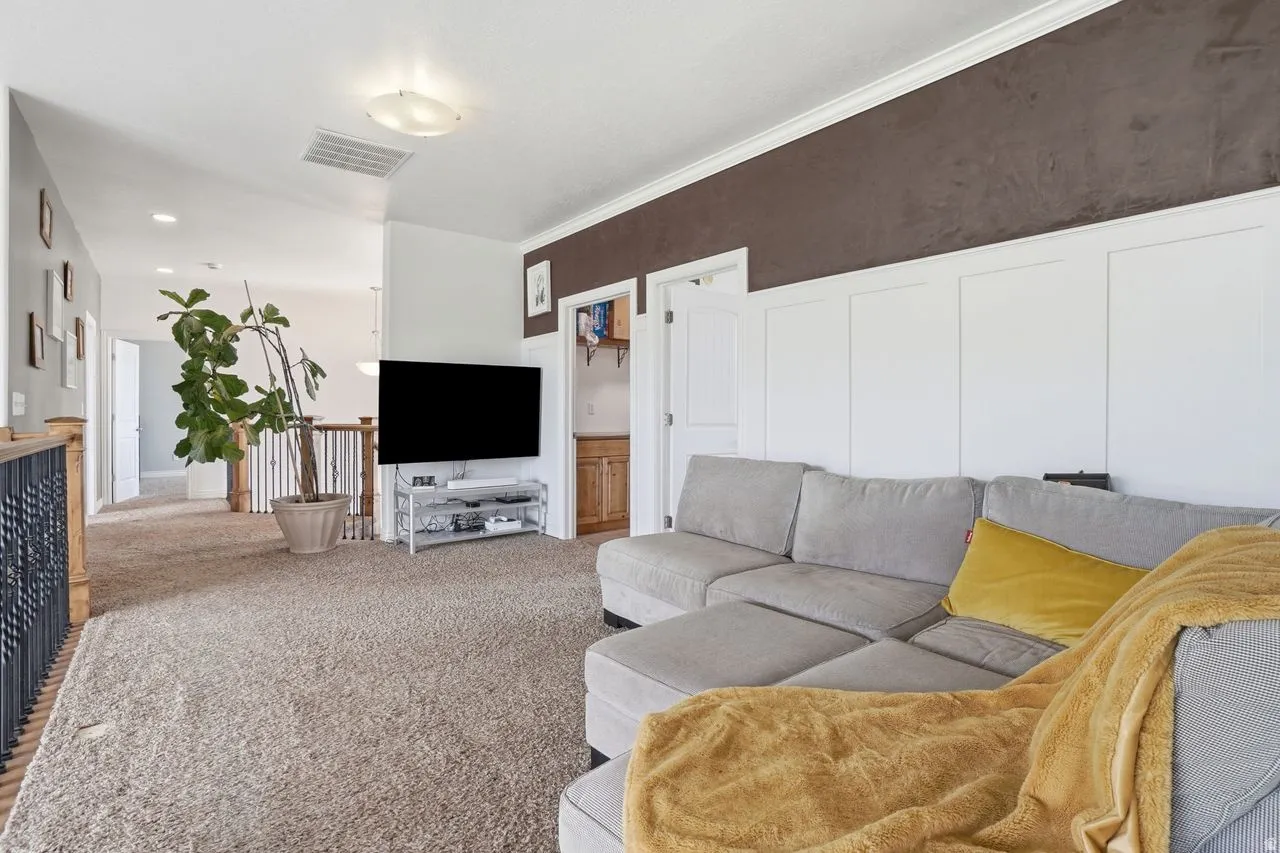 Carpeted room with a textured accent wall, crown molding, and wainscoting