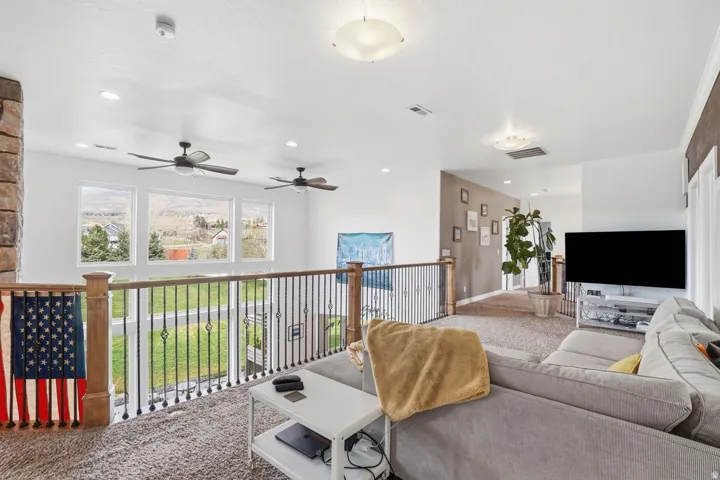 Open concept loft space featuring a stone-clad pillar, decorative metal railing, recessed lighting, and multiple ceiling fans