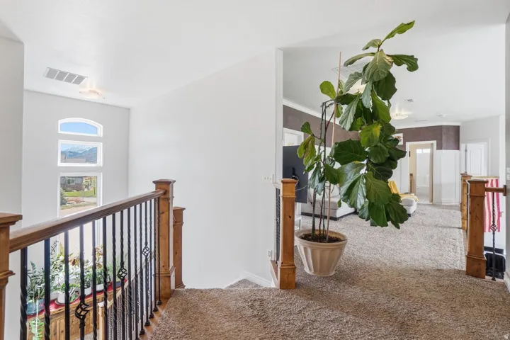 Carpeted upper landing featuring a wood and wrought iron railing, arched window, and recessed lighting