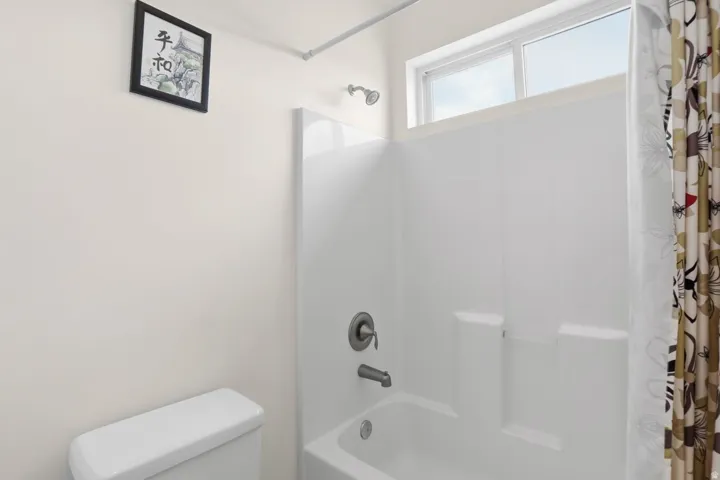 White toilet, white shower/tub combination, overhead window, and wall-mounted shower head