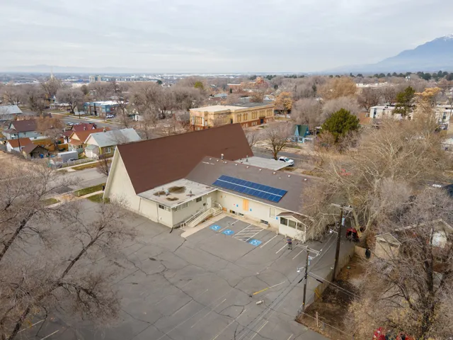 Building with a brown shingle roof, solar panels, and a large asphalt parking lot