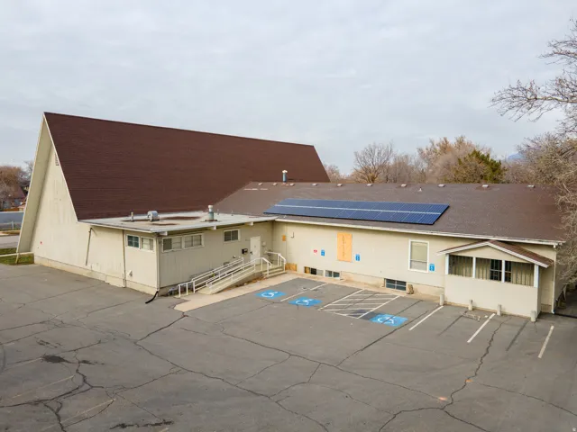 Expansive asphalt parking lot, large commercial building with a brown shingle roof, solar panel array, covered entrance, and an accessible ramp