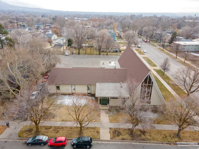 Gable roof structure with a prominent glass facade, expansive paved parking lot, and a flat roof section