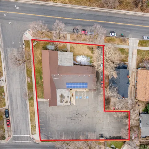 Asphalt parking lot with marked spaces, building with multiple roof sections, solar panel array, and street frontage
