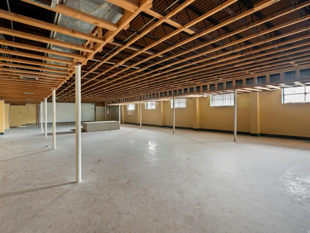 Spacious unfinished basement with exposed wood-beam ceiling structure, concrete flooring, and abundant natural light from multiple high windows