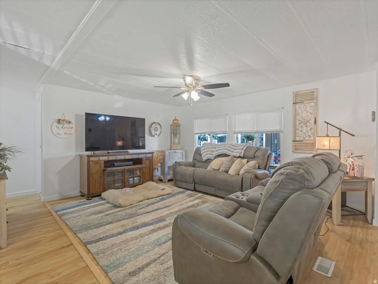Wood-finish flooring, white walls, multiple windows with blinds, and a ceiling fan with integrated lighting