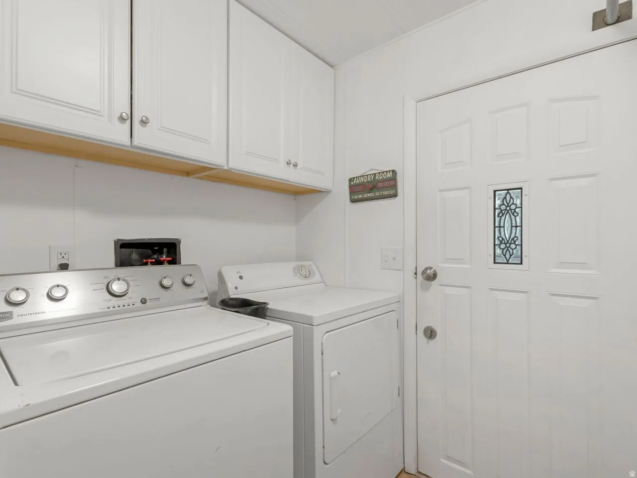 White shaker-style upper cabinetry with silver-tone hardware, white paneled door with decorative glass insert, and a built-in shelf