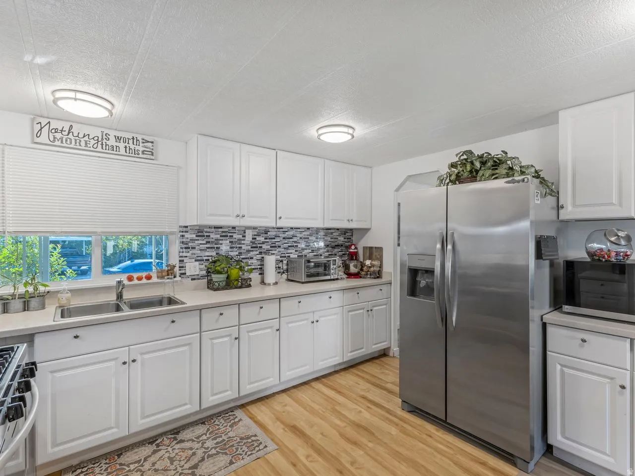 White cabinetry, wood-finish flooring, mosaic tile backsplash, stainless steel refrigerator, and recessed lighting