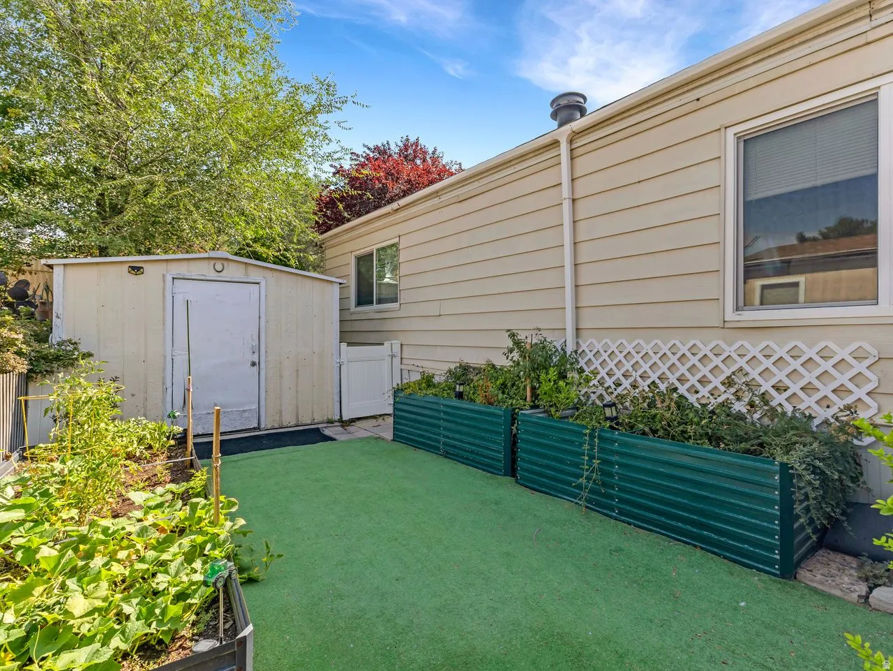 Green corrugated metal planters, artificial turf, white lattice detailing, and a metal storage shed