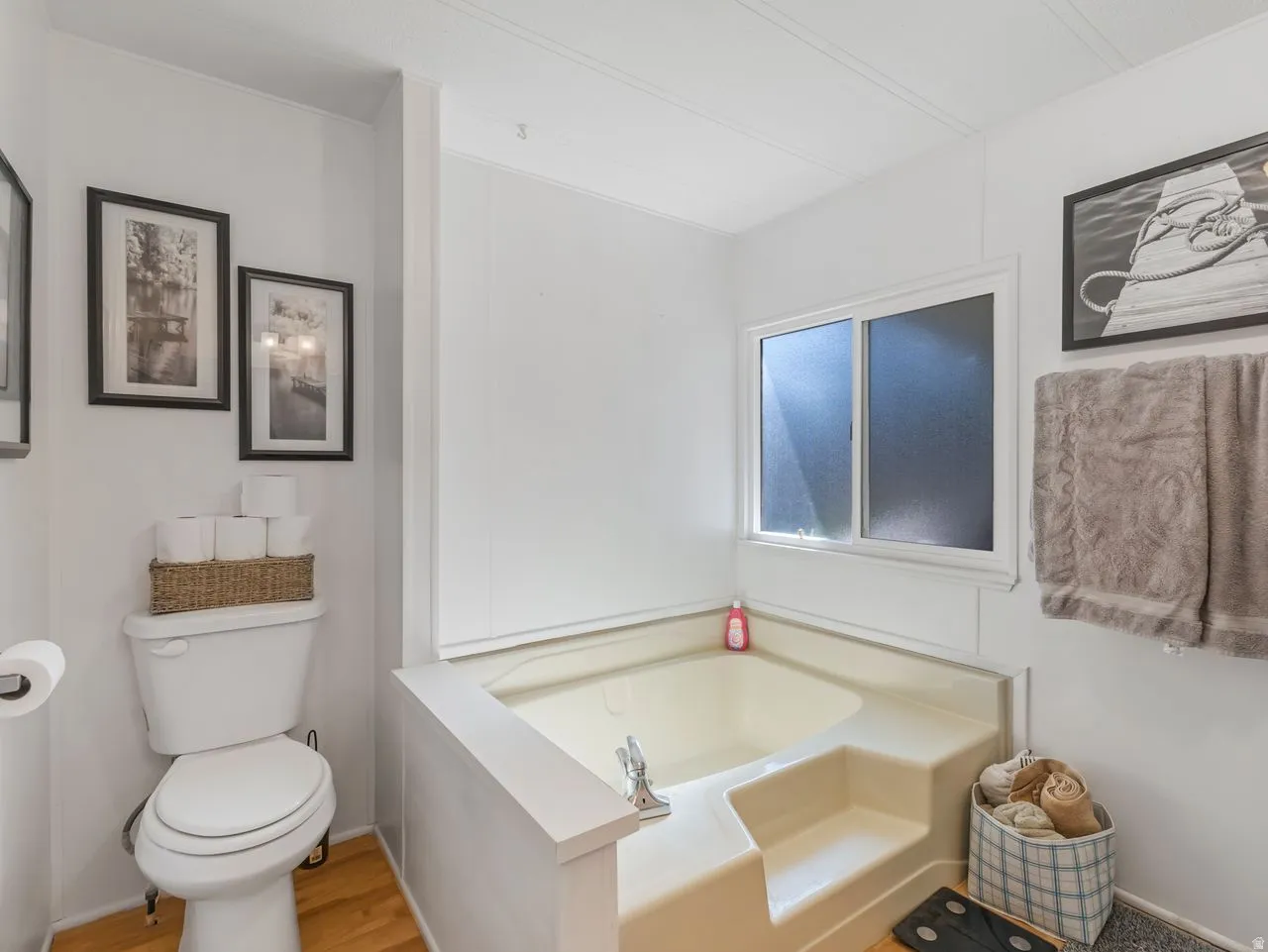 Built-in corner soaking tub with integrated steps, white walls, and wood-finish flooring