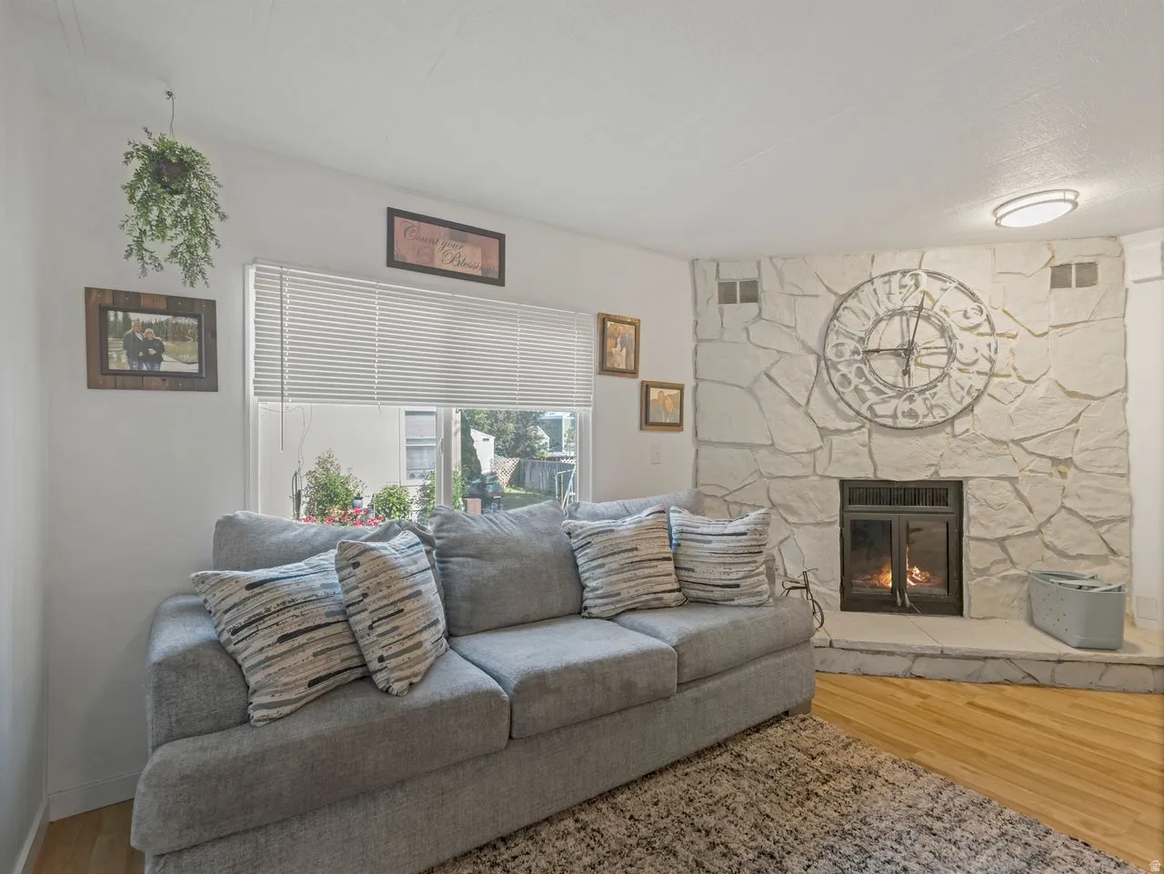 Stone-clad fireplace with a hearth, wood-finish flooring, and natural light from the window
