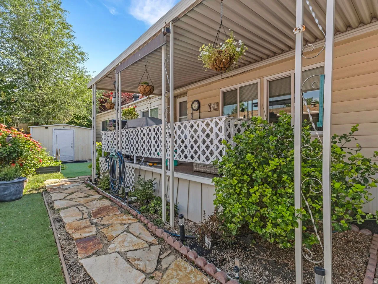 Covered patio with lattice railing, flagstone pathway, detached storage shed, and mature landscaping