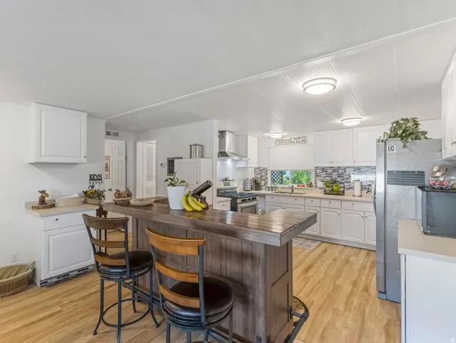 Kitchen featuring a rustic wood-finish island with seating, white cabinetry, light countertops, wood-finish flooring, and stainless steel appliances