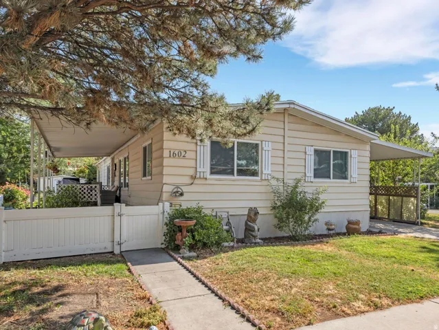 Single-story residence featuring horizontal siding, white window shutters, a covered patio, a covered carport, and a white picket fence