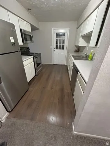 Kitchen featuring wood-finish flooring, white cabinetry, stainless steel appliances, and a glass-paneled door