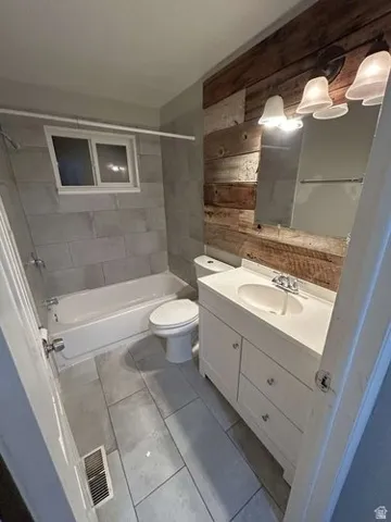 Bathroom featuring a white vanity with integrated sink, a three-light fixture, a wood-panel accent wall, subway tile shower surround, and tile flooring