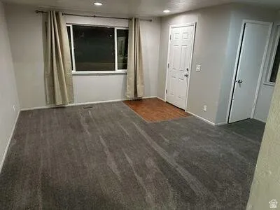 Recessed lighting, light gray wall paint, window with white trim, wood-finish flooring at entry, and neutral carpeting