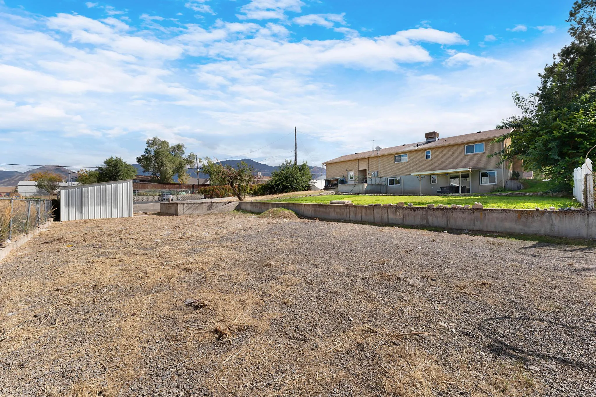 Expansive gravel area with a retaining wall and partially visible residential structure