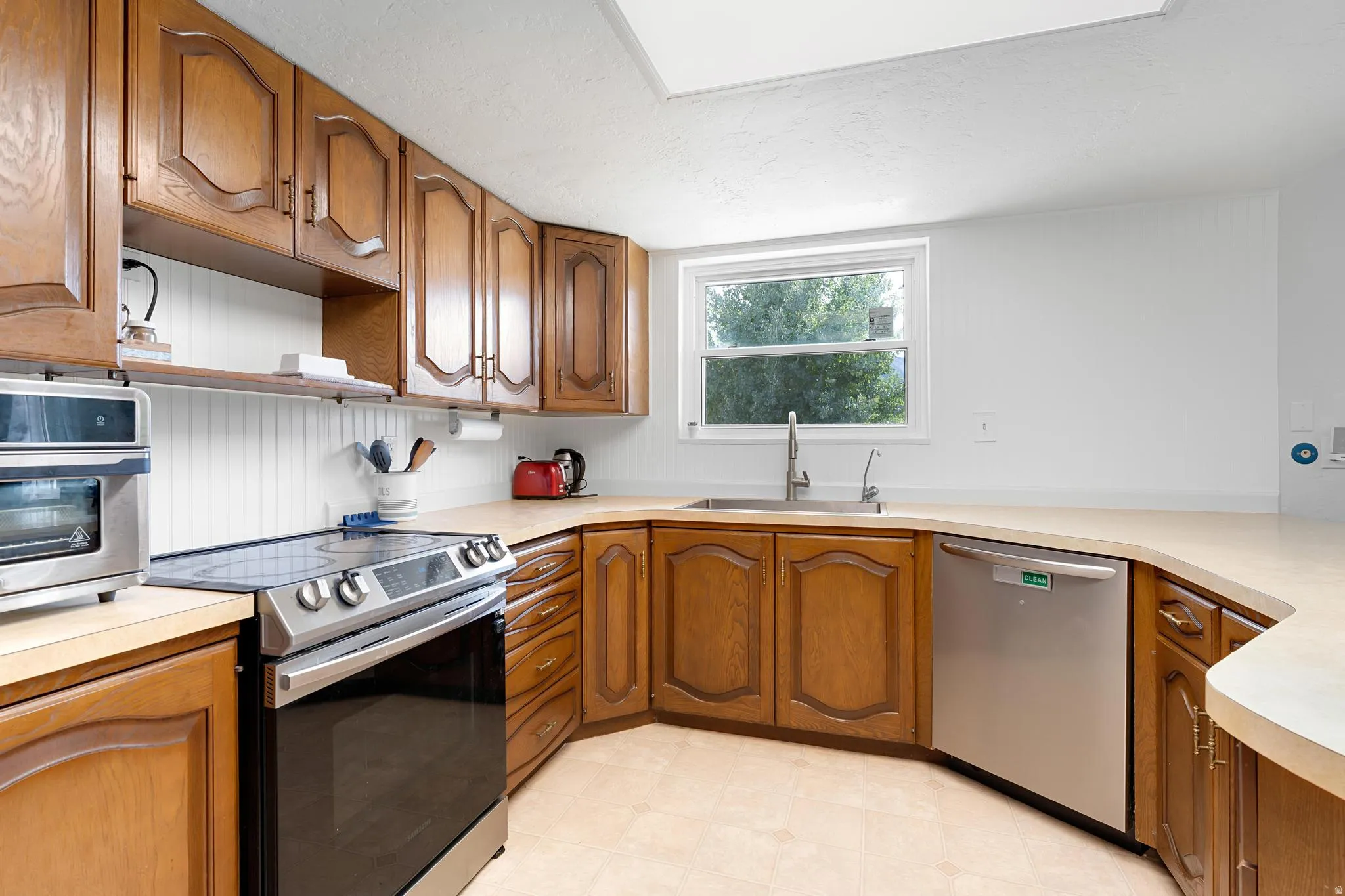 Wood-finish cabinetry, light-toned countertops, a stainless steel dishwasher, a stainless steel range, and a window above the sink