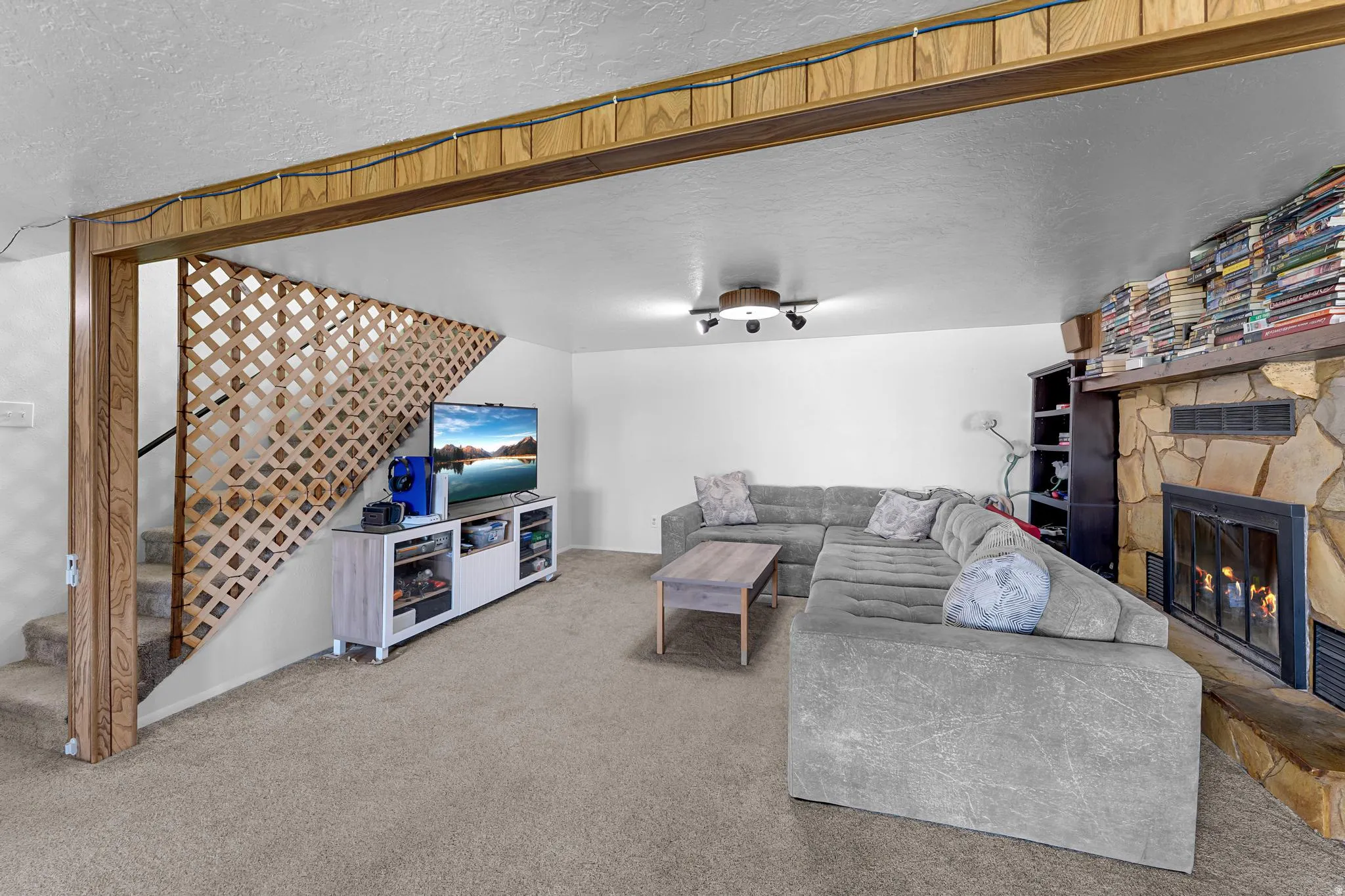 Built-in stone fireplace with hearth, wood-finish ceiling beams, and a lattice staircase railing